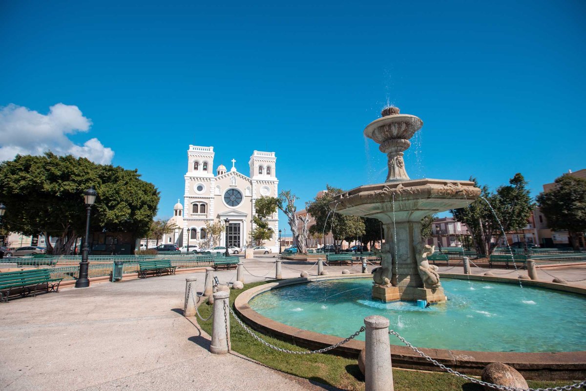 A view of the main town square of Guayama, Puerto Rico, which includes a fountain and historic church.