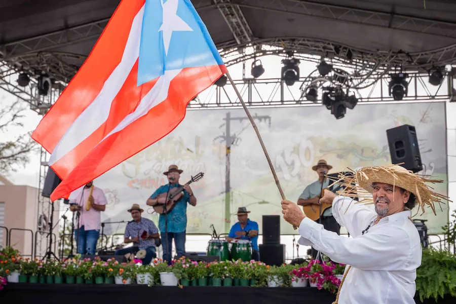 Persona con vestimenta tradicional sosteniendo la bandera de Puerto Rico.