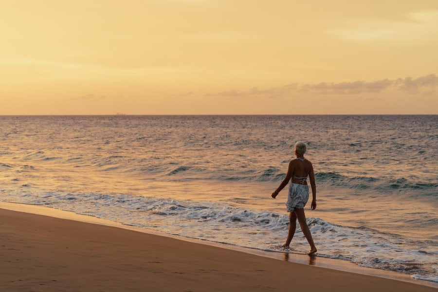 A woman walks along the shoreline at sunset, with gentle waves and golden light reflecting off the water on a peaceful Puerto Rican beach.