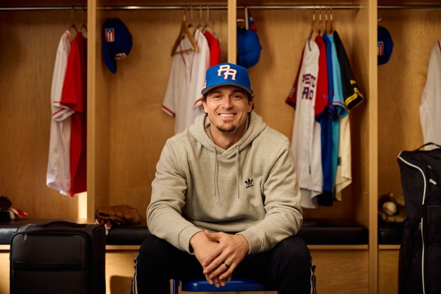 Baseball player Kike Hernandez sits in a locker room with Puerto Rico's basbeball hat.