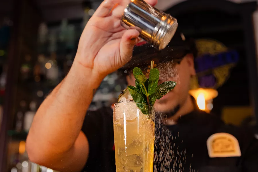Mixologist sprinkling garnish on top of a cocktail.