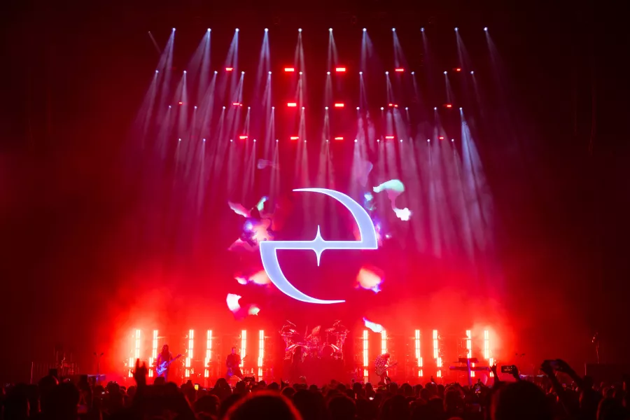 Rock concert with a large crowd and a red illuminated stage featuring a glowing logo above the band.