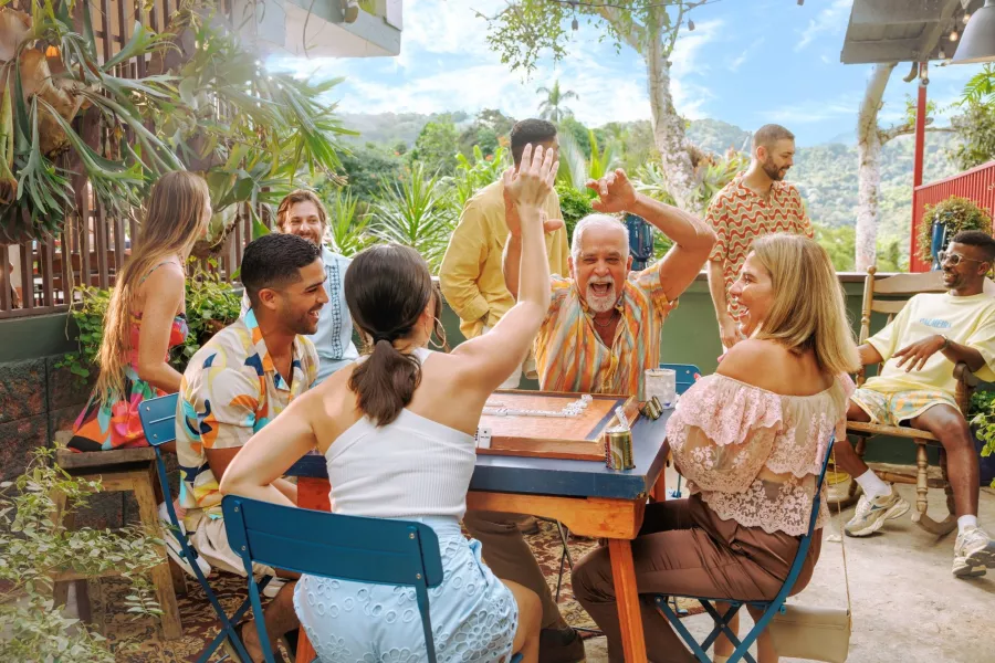 Group of friends and family laughing and celebrating around a table during an outdoor gathering in Puerto Rico, surrounded by lush greenery and mountain views.