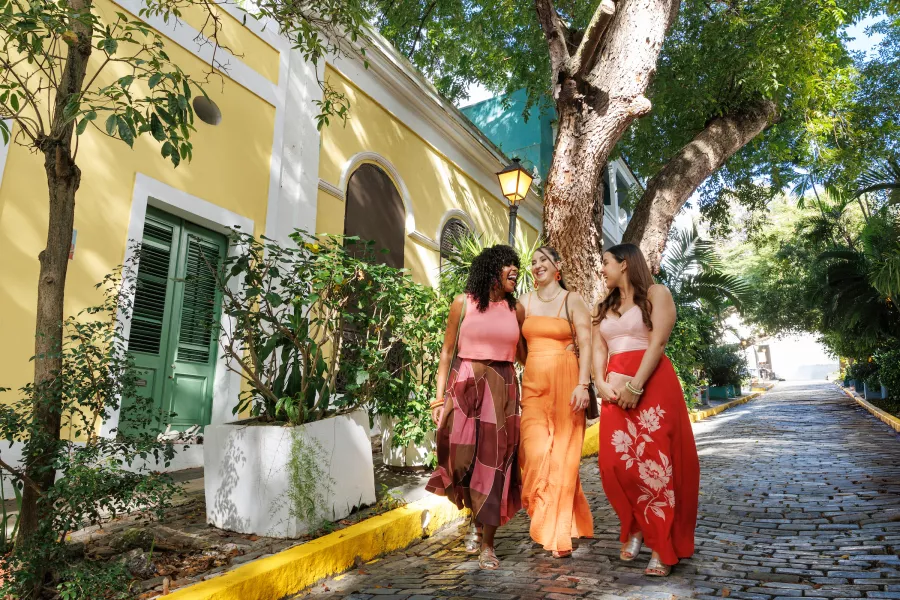 Three women walking on a cobblestone street in Old San Juan wearing colorful outfits from Valija.