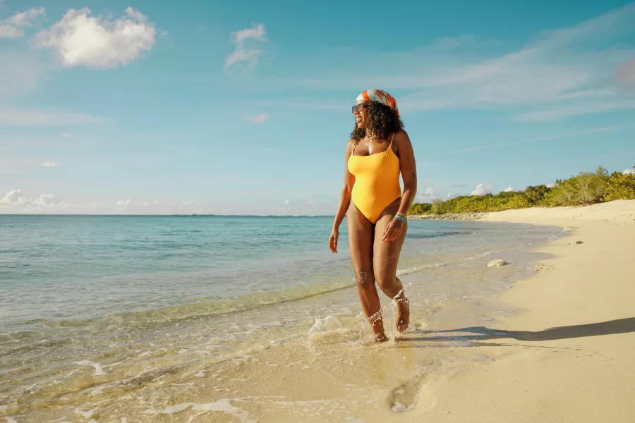 Woman walking along a beach wearing a yellow swimsuit and a colorful headscarf