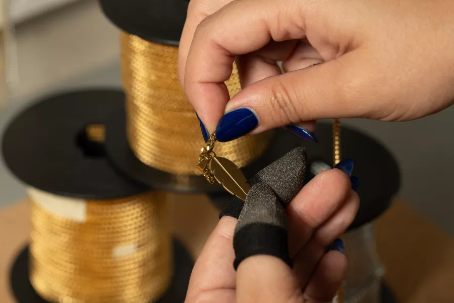 Close-up of jewelry-making process with gold chains and pendant