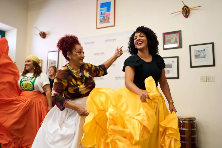 Two women smile while dancing Bomba in flowing traditional skirts during a cultural dance workshop in Puerto Rico.