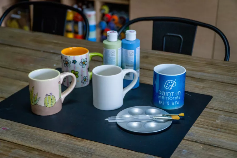 Ceramic mugs, paintbrushes, and paints arranged on a table at Paint in Memories in Puerto Rico.