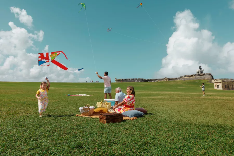 Family enjoying a picnic while a child flies a kite on the lawn overlooking El Morro in Old San Juan, Puerto Rico.