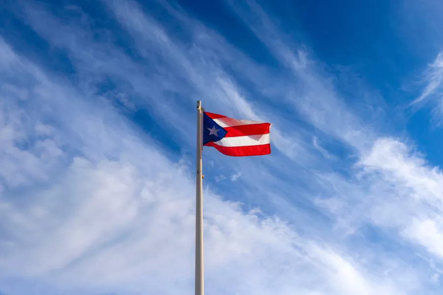 Puerto Rican flag waving on a flagpole against a blue sky with wispy clouds.