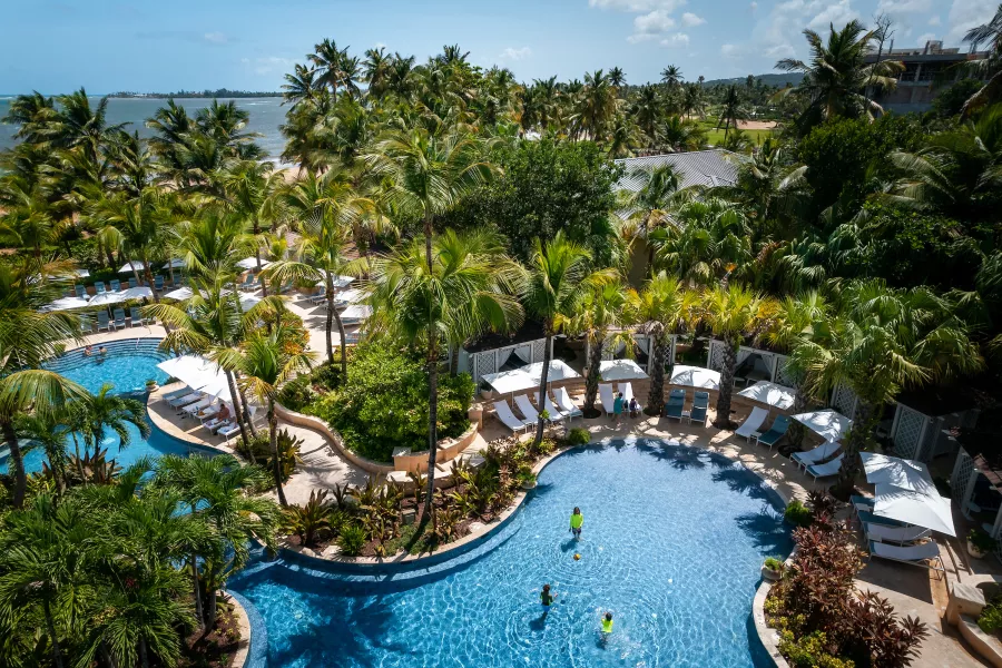 Aerial view of Four Seasons Resort and Residences Puerto Rico with two swimming pools surrounded by palm trees, gardens, and a nearby beach.