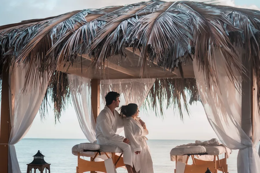 Pareja disfrutando de un tratamiento de spa en una cabaña con techo de paja y vistas al mar Caribe en Copamarina Beach Resort & Spa.