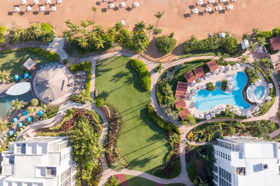 Vista aérea de la piscina del Wyndham Grand Rio Mar, rodeada de palmeras, jardines, sillas reclinables y exuberantes áreas tropicales.