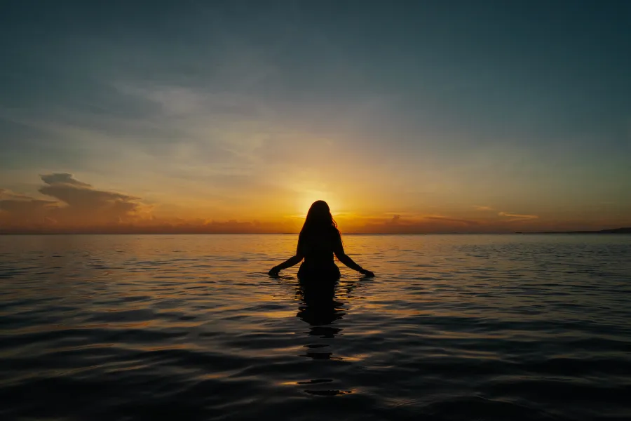 Person standing waist-deep in the ocean at sunset during Noche de San Juan in Puerto Rico.