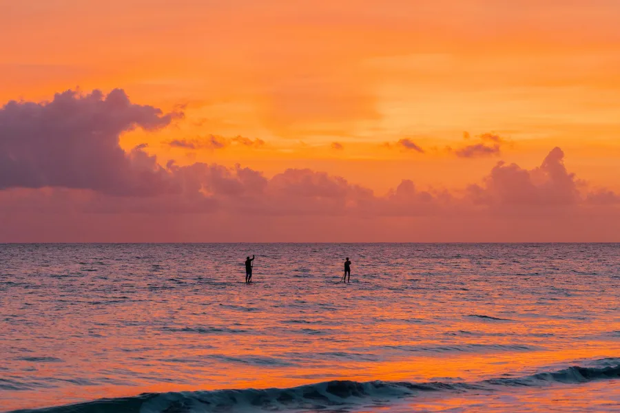 Sunset over the ocean in Puerto Rico with two people standing in the water during Noche de San Juan.
