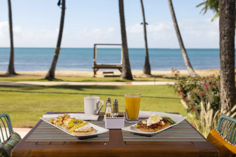 Two plates of breakfast food with a cup of coffee and orange juice situated on the open-air back patio at Las Palmas Café in Guánica.