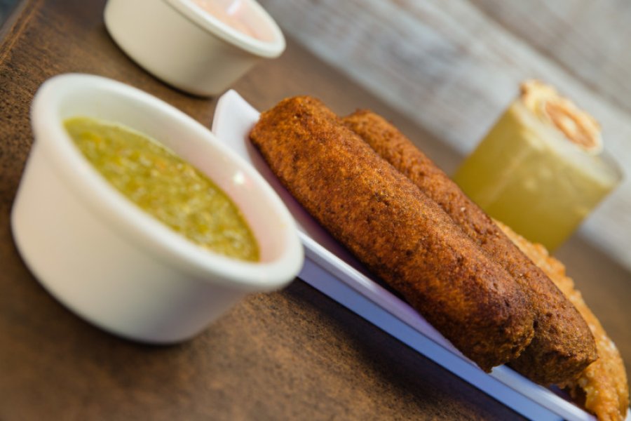 A plate of alcapurria fritters with a bowl of green sauce.