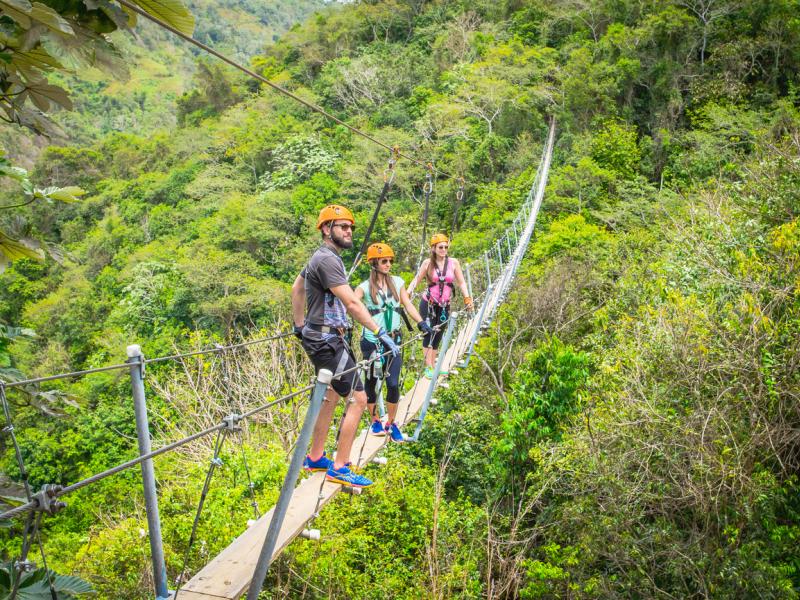 Three people stand on a suspended bridge above the forest at Toro Verde Adventure Park.