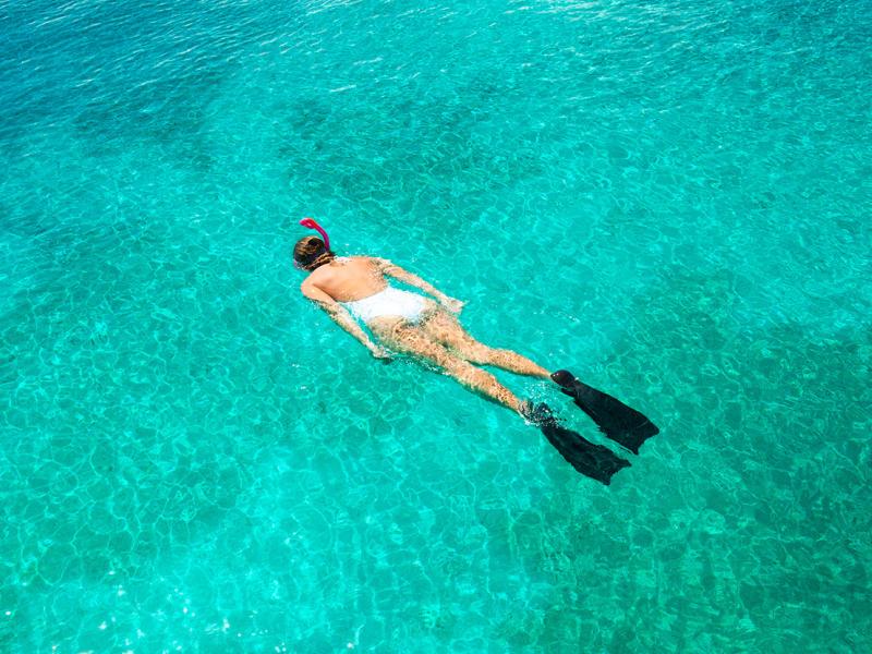 Woman snorkeling in white bathing suit against turquoise waters. 