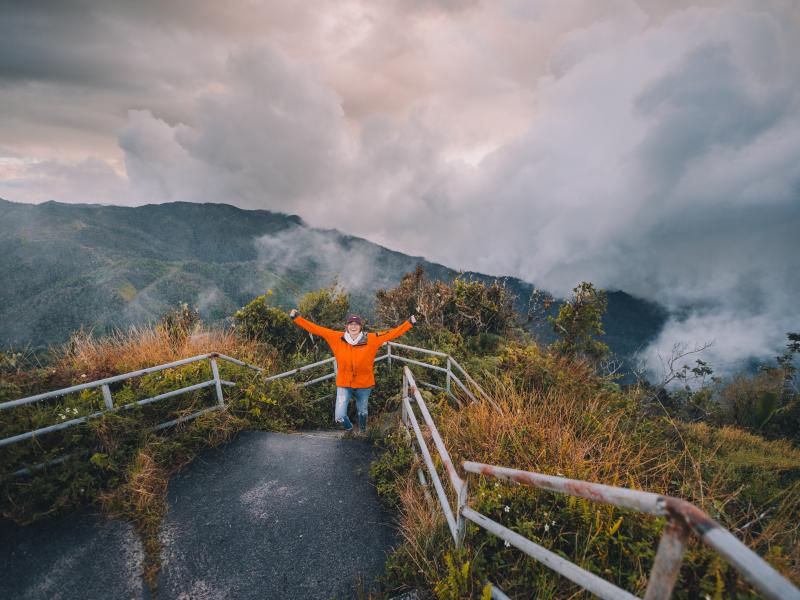 A woman raises her arms triumphantly after hiking up the side of a mountain.