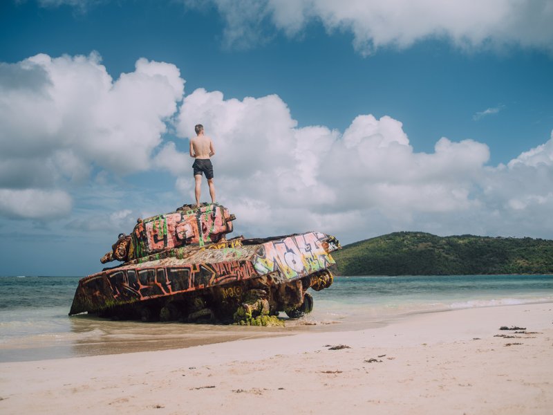 A man stands at the top of an abandoned war tank in Flamenco Beach 