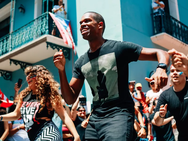 Personas bailando en las calles del Viejo San Juan, celebrando los bailes típicos de Puerto Rico.