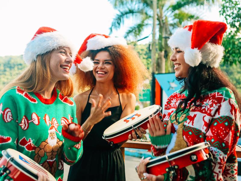 Three young ladies wearing Santa hats and Christmas sweaters playing the pandero, a typical instrument of Puerto Rico's Christmas parrandas.