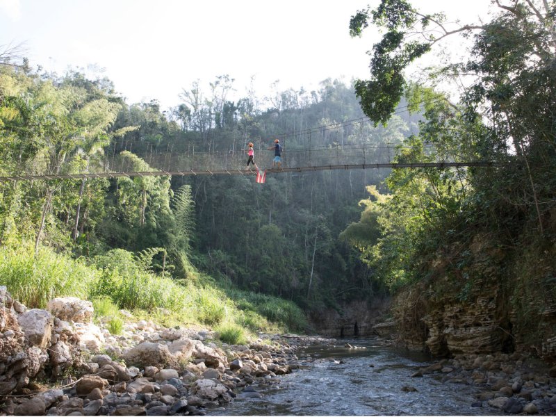 A pair of travelers walk over a bridge on the Tanama River in Utuado, Puerto Rico.