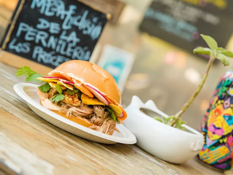 Un sándwich con muchos aderezos y una colorida lata de cerveza se muestran en una mesa en Lote 23, un parque de camiones de comida en el barrio de Santurce de San Juan, Puerto Rico.