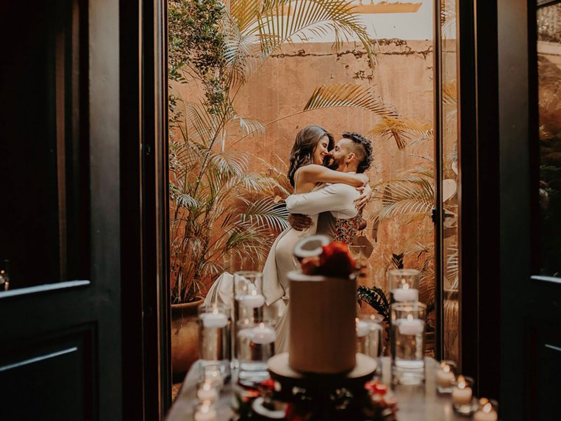 A couple embraces on a balcony with a wedding cake in the foreground at El Convento in San Juan, Puerto Rico.