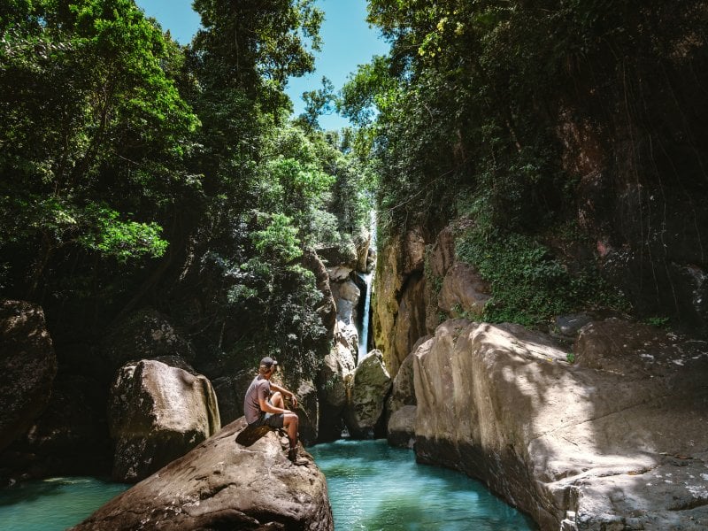 Hiker standing in front of a waterfall in El Yunque National Forest, Puerto Rico rainforest adventure.