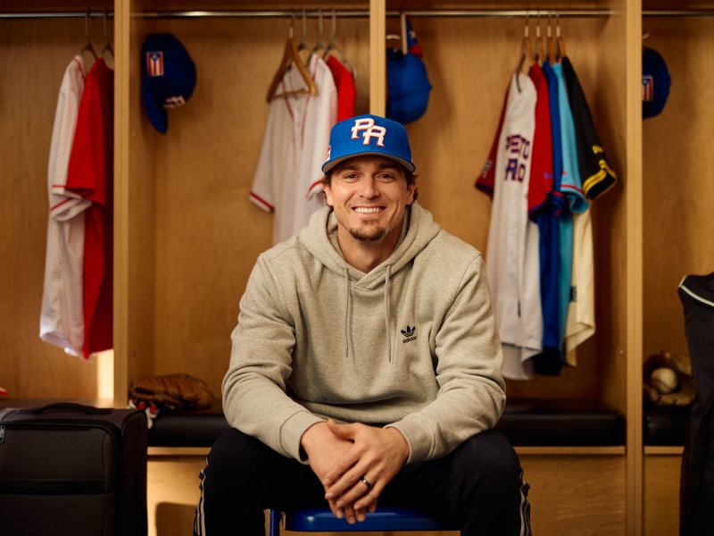 Baseball player Kike Hernandez sits in a locker room with Puerto Rico's basbeball hat. 