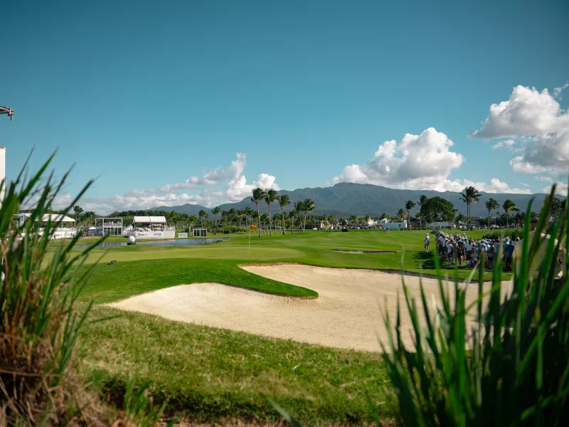 "Scenic view of the Grand Reserve Golf Club with a sand bunker and green in the foreground, palm trees and mountains in the background.