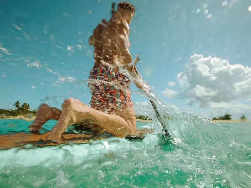 Man paddleboarding through clear turquoise water on Puerto Rico’s east coast, splashing waves near a tropical shoreline under a bright blue sky.