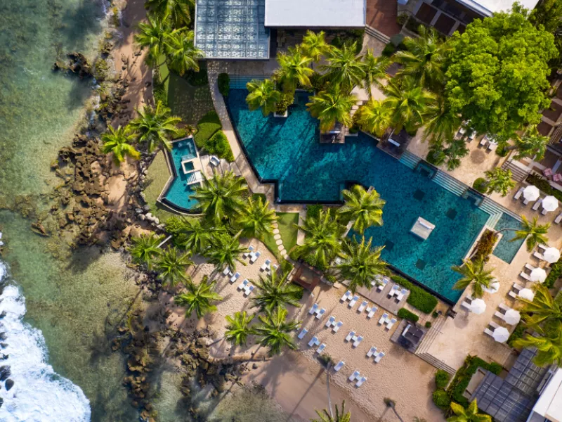 Aerial view of Dorado Beach, a Ritz-Carlton Reserve, featuring oceanfront pools, palm trees, lounge chairs, and a sandy beach along Puerto Rico's coast.
