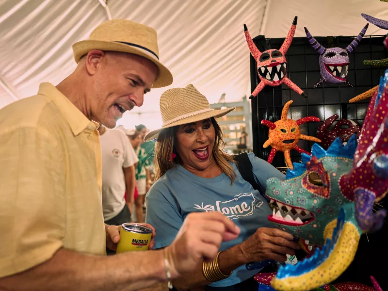 Visitors browse colorful handcrafted vejigante masks and artisan creations at a cultural market in Puerto Rico, celebrating the Island’s rich artistic traditions and craftsmanship.