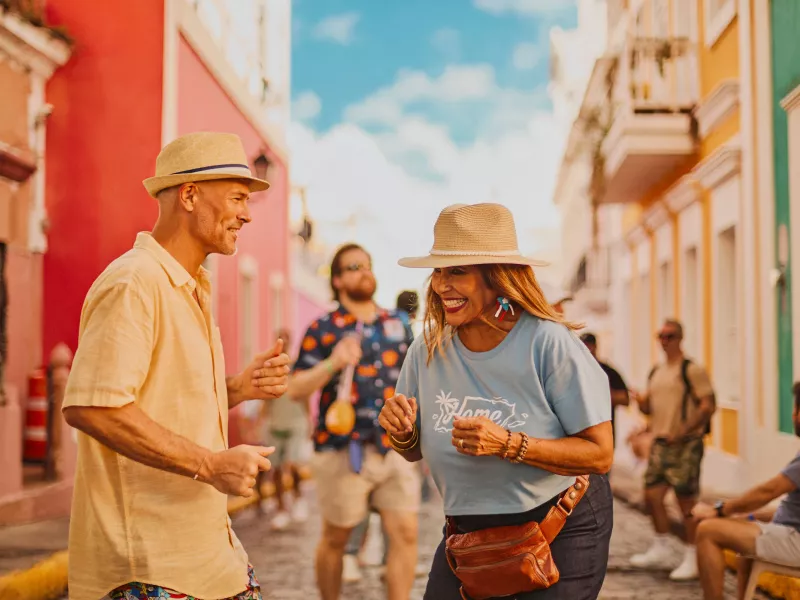 Two people smiling and dancing together on a colorful street in Old San Juan during the Fiestas de la Calle San Sebastián in Puerto Rico.