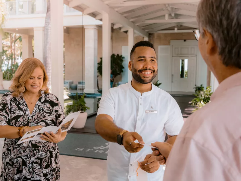 Un miembro del personal da la bienvenida a los huéspedes a su llegada a Four Seasons Resort and Residences Puerto Rico, destacando el servicio personalizado y la hospitalidad de lujo que distinguen a este resort frente al mar.