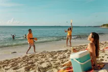 Friends playing paddleball and relaxing on a sandy beach along Puerto Rico’s east coast, with others swimming in the clear turquoise water under a sunny sky.