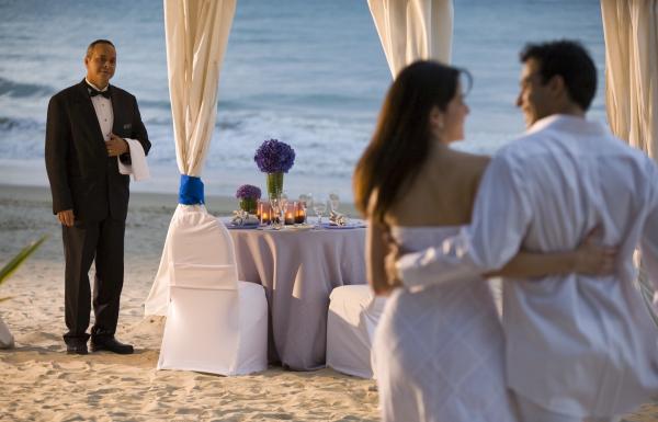 A couple walks on the beach towards a waiting dinner table.