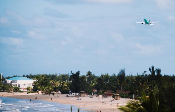 A plane departs from an airport over a beautiful beach.