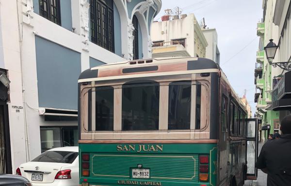 A green bus drives on a historic street in Old San Juan.