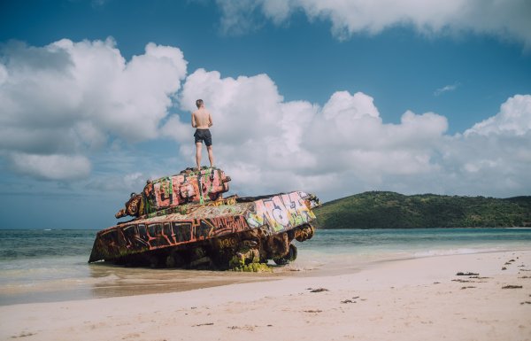 A man stands at the top of an abandoned war tank in Flamenco Beach