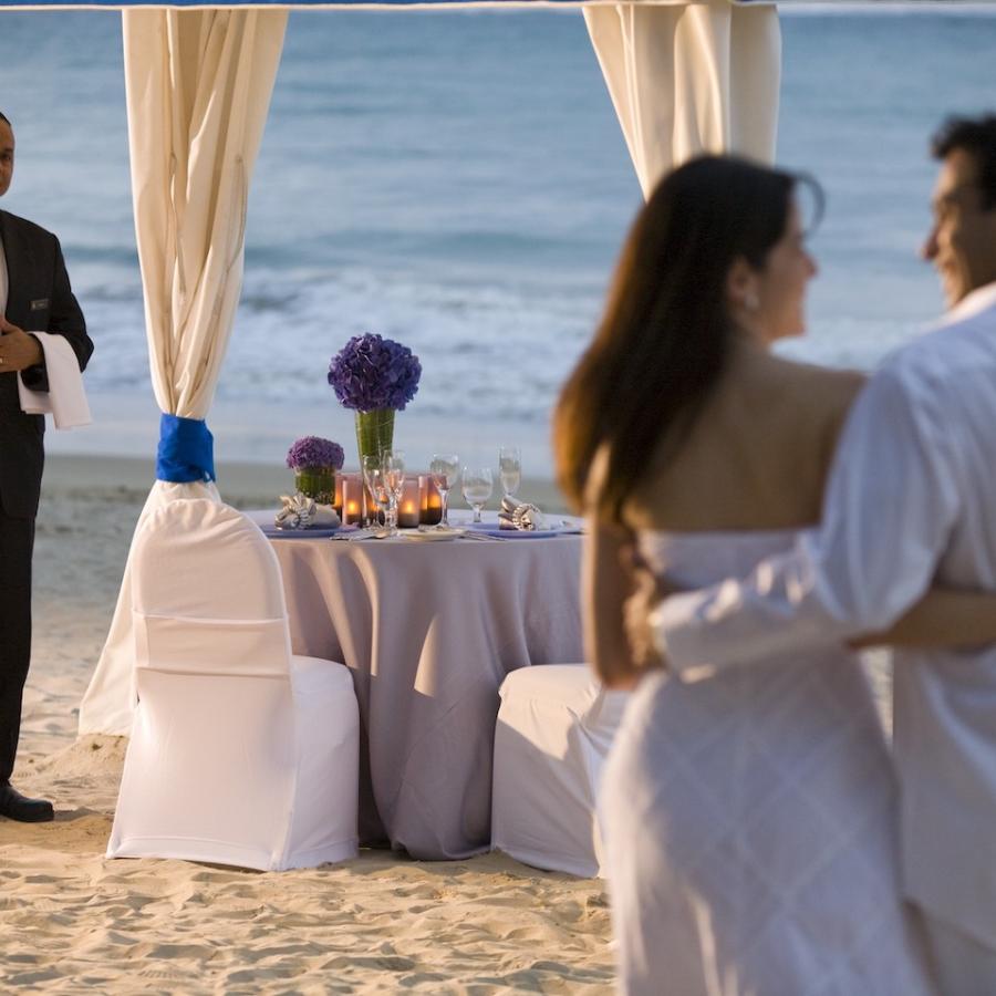 A couple walks on the beach towards a waiting dinner table.