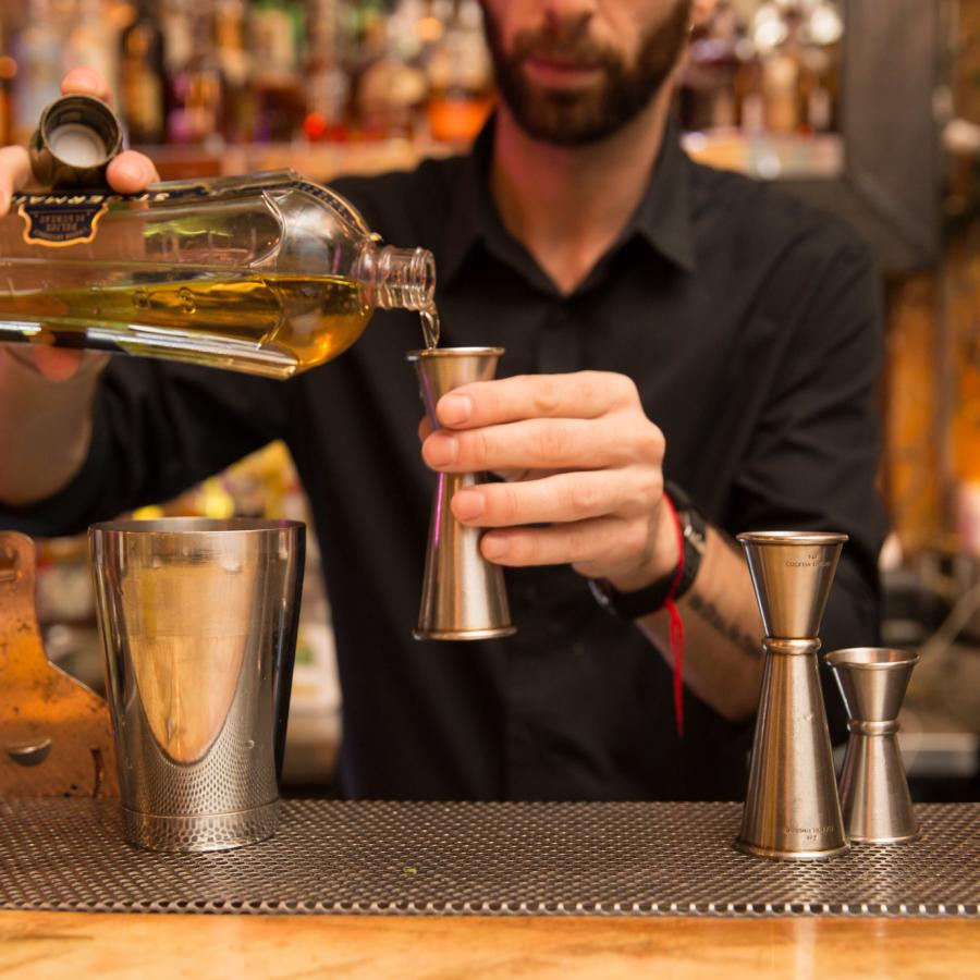 A bartender measures a pour of liqueur for a cocktail
