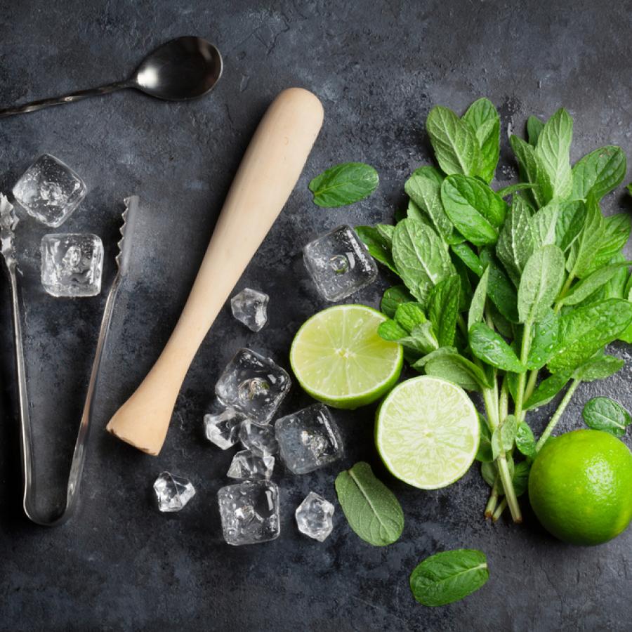 A display of mint leaves, limes, and cocktail tools for making mojitos.