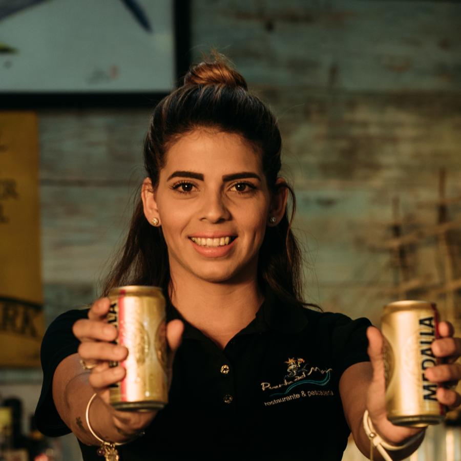 A bartender in San Juan holding two cans of Medalla.