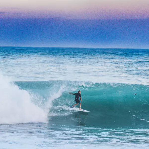 Silhouetted against a vibrant sunset, a skilled surfer rides a barreling wave in Puerto Rico, showcasing the thrill of its surf.