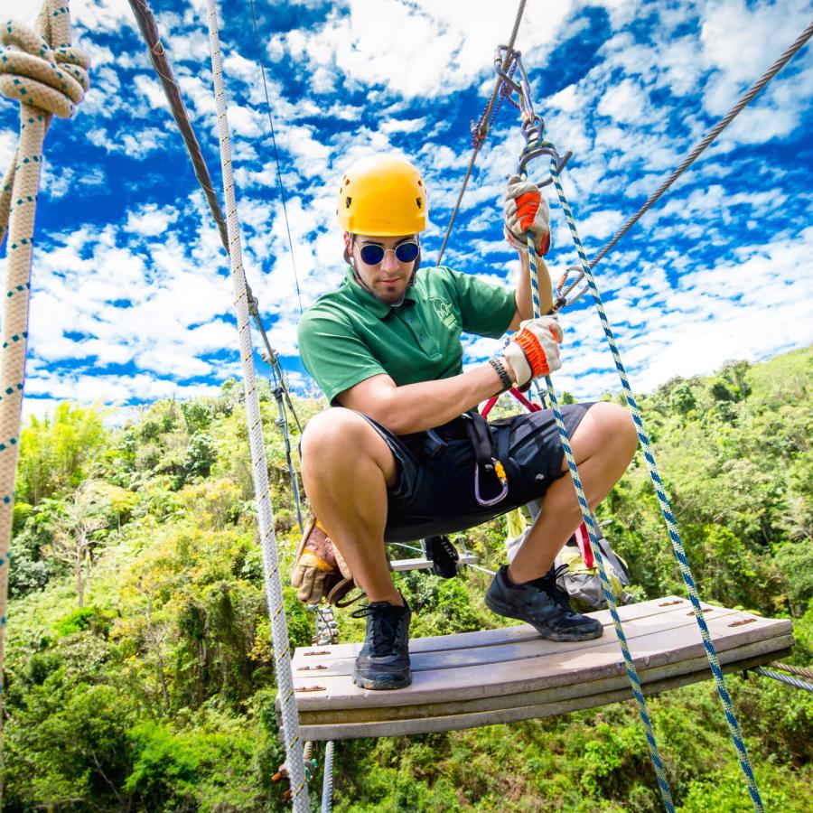 Man crouching on a suspension bridge at Toro Verde Zipline. 