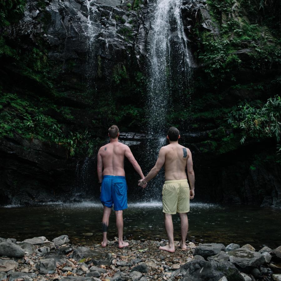 A gay couple stands together looking up at a waterfall